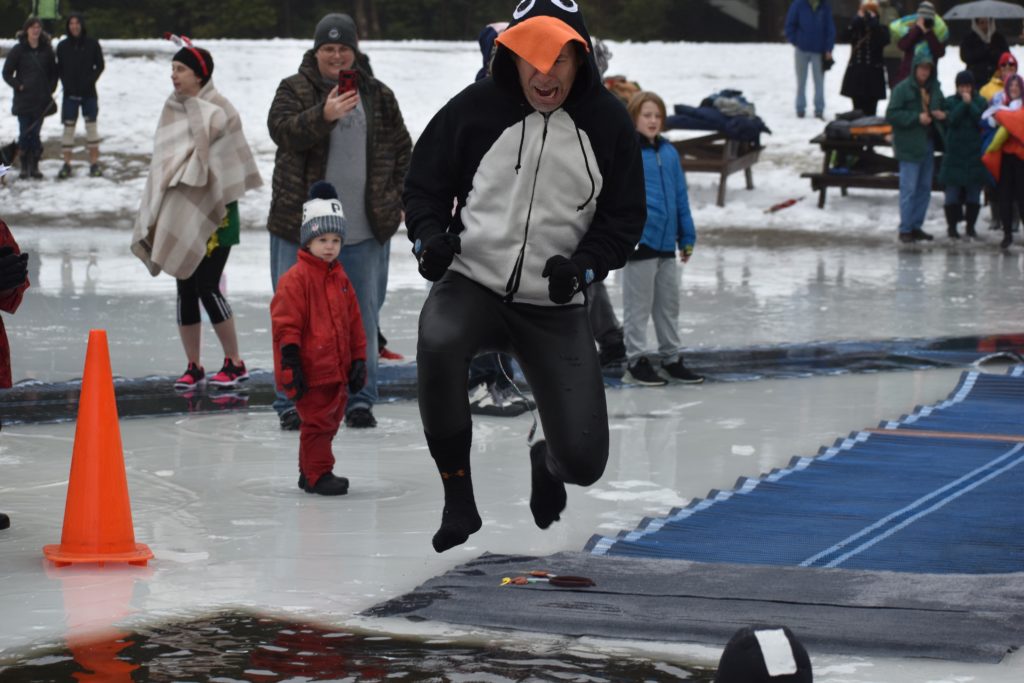 man in a penguin costume in mid-air jumping into the lake