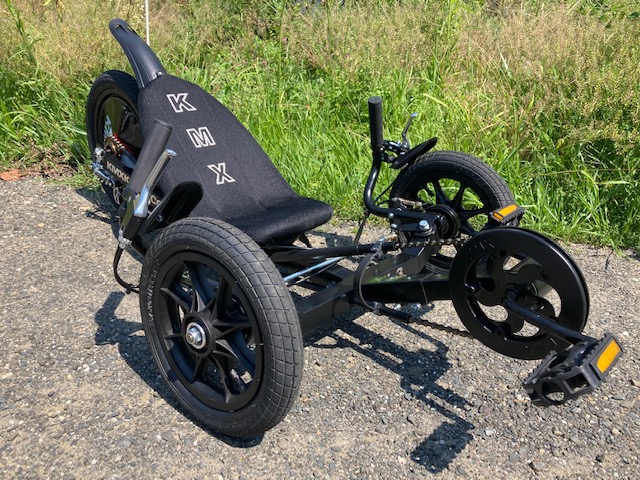 Small black tricycle with reclined seat and the letters "K M X" going vertically down the seat 