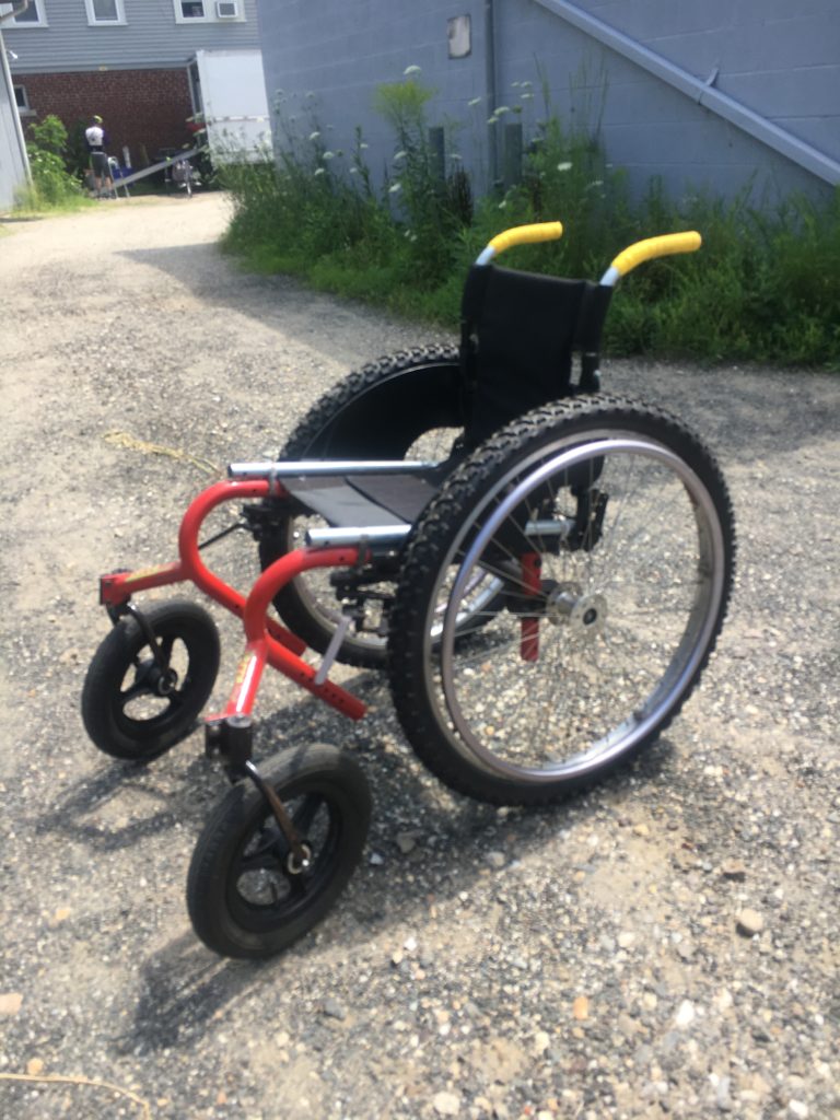A small, red wheelchair with thick tires and front casters. 