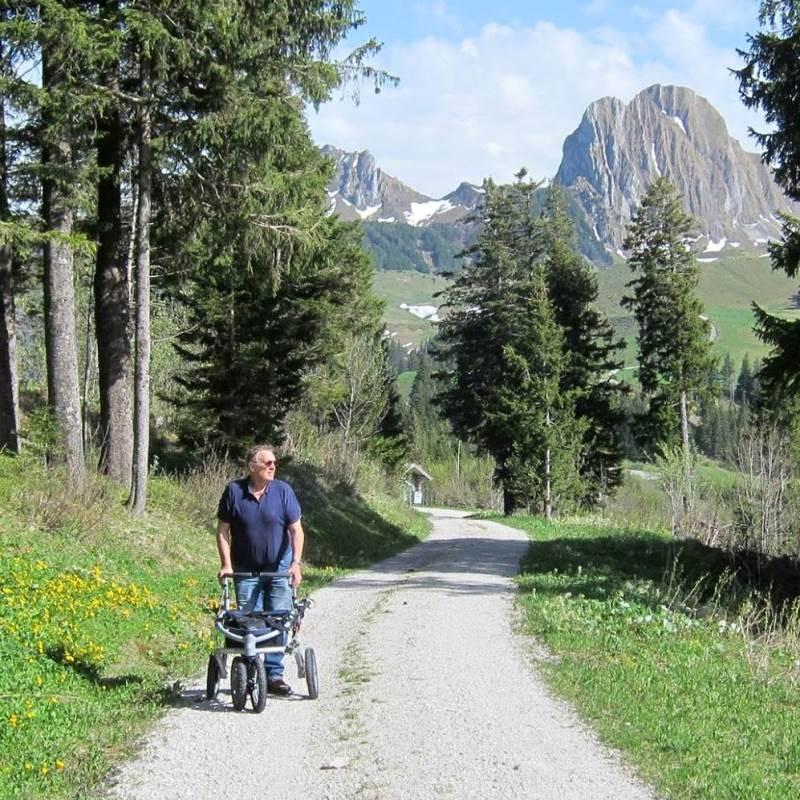 A tall masculine person using the walker to walk on gravel trails in the mountains 