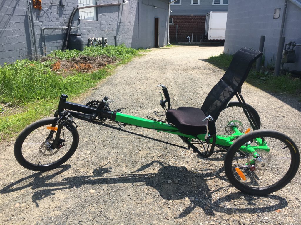 Green recumbent trike with one wheel in the front and two wheels in the back. 