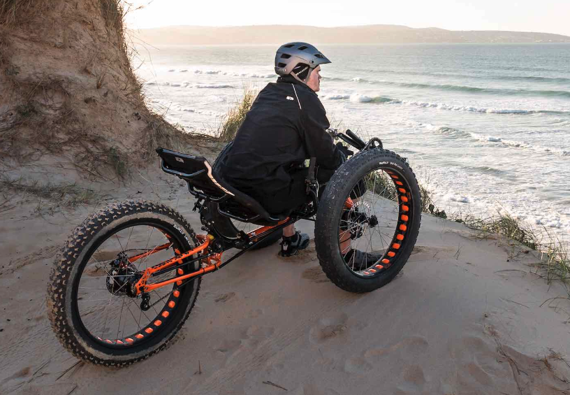 A person sitting on the trike taking a rest overlooking the ocean. The trike is on beach sand. 