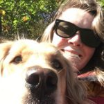 A woman with sunglasses smiling with a golden retreiver dog